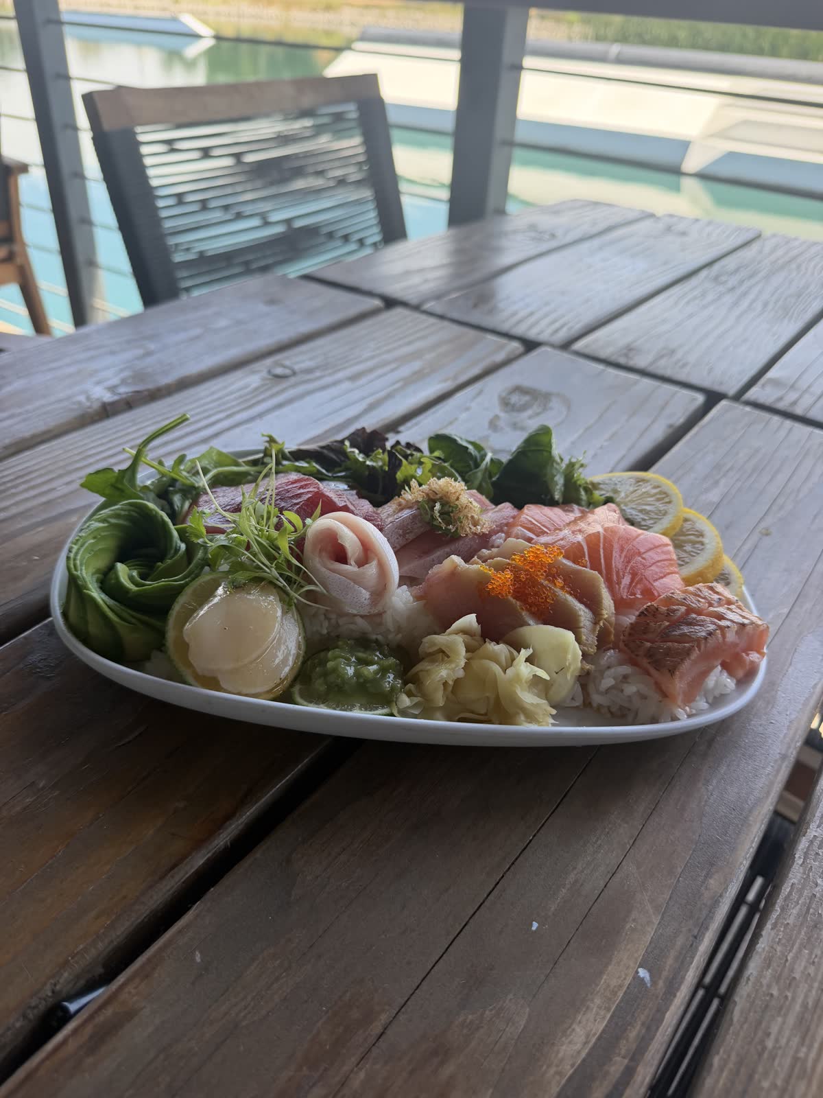 Chirashi platter with fresh greens and garnish on a weathered deck table at Costa Fuego